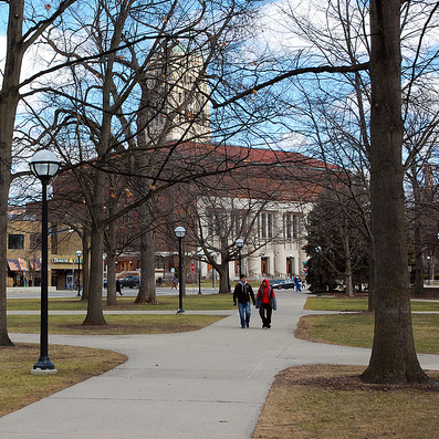 photo of 2 people walking with Hill Auditorium and the Bell Tower in the background