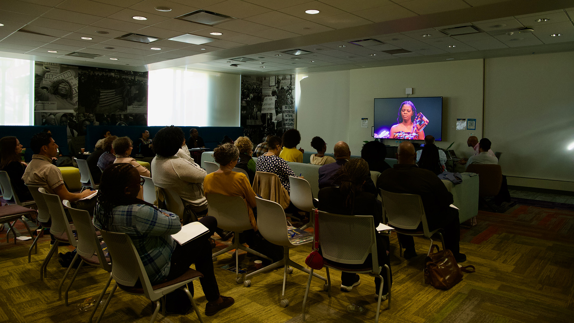 Audience facing a monitor watch the How Do We Begin film