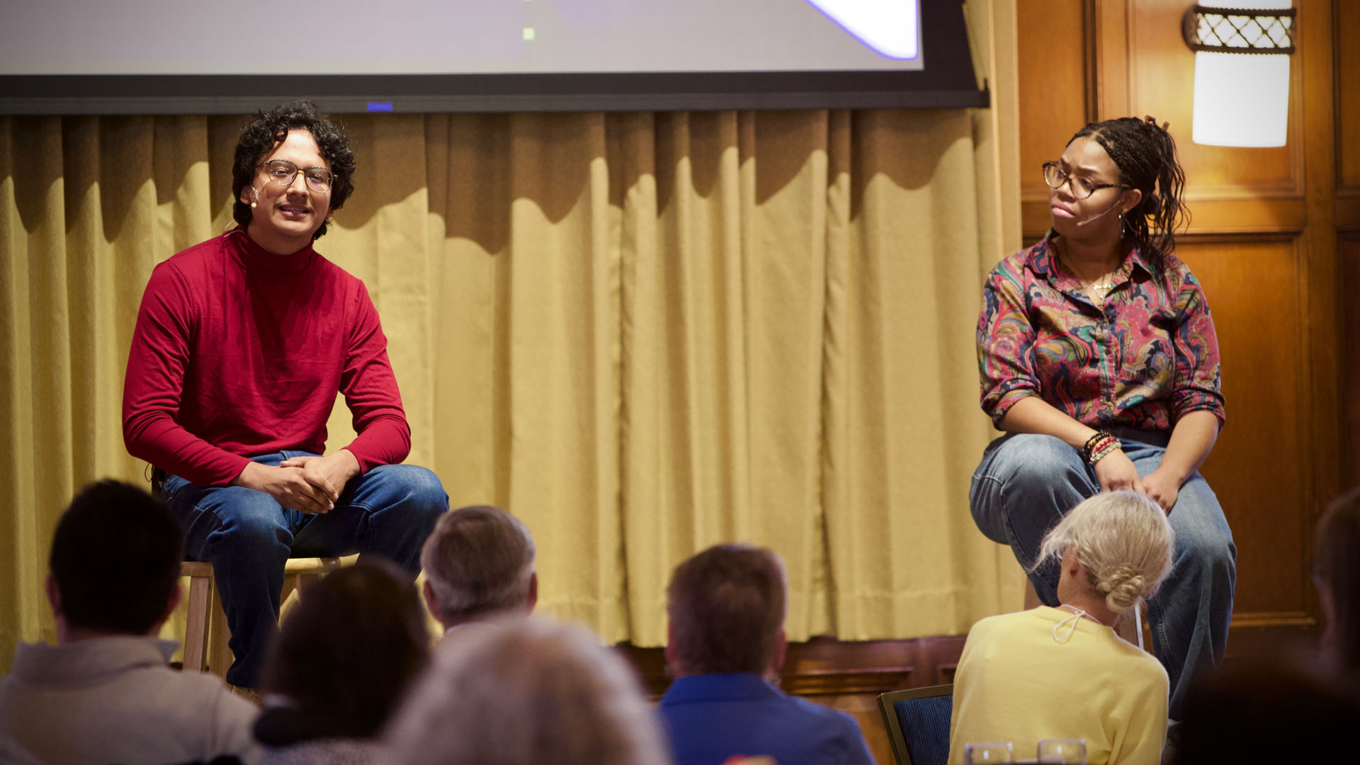 Two performers seating on stools facing an audience
